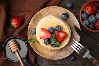 Photo of Delicious pancakes with strawberries, blueberries and mint served on wooden table, flat lay