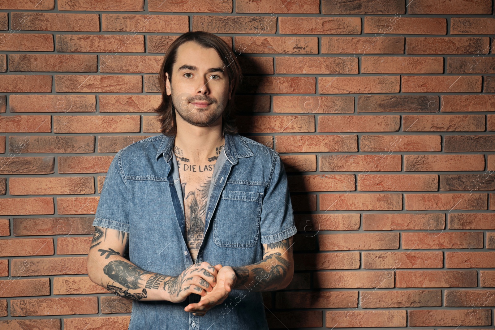 Photo of Young man with tattoos on body near brick wall