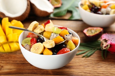 Delicious exotic fruit salad and ingredients on wooden table