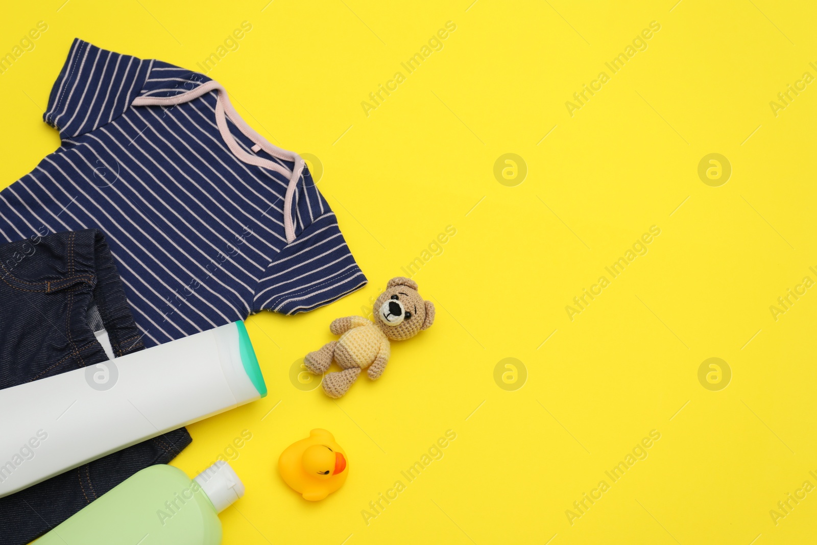 Photo of Bottles of laundry detergents, baby clothes and toy bear on yellow background, flat lay. Space for text