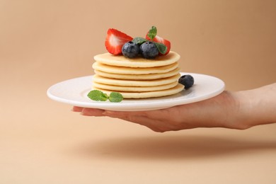 Photo of Woman holding delicious pancakes with strawberries, blueberries and mint against dark beige background, closeup