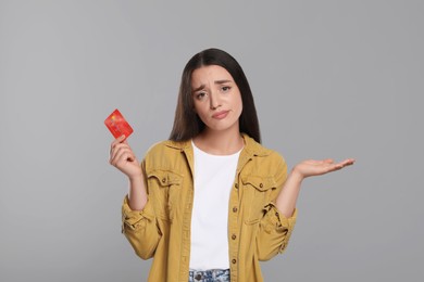 Confused woman with credit card on light gray background. Debt limit