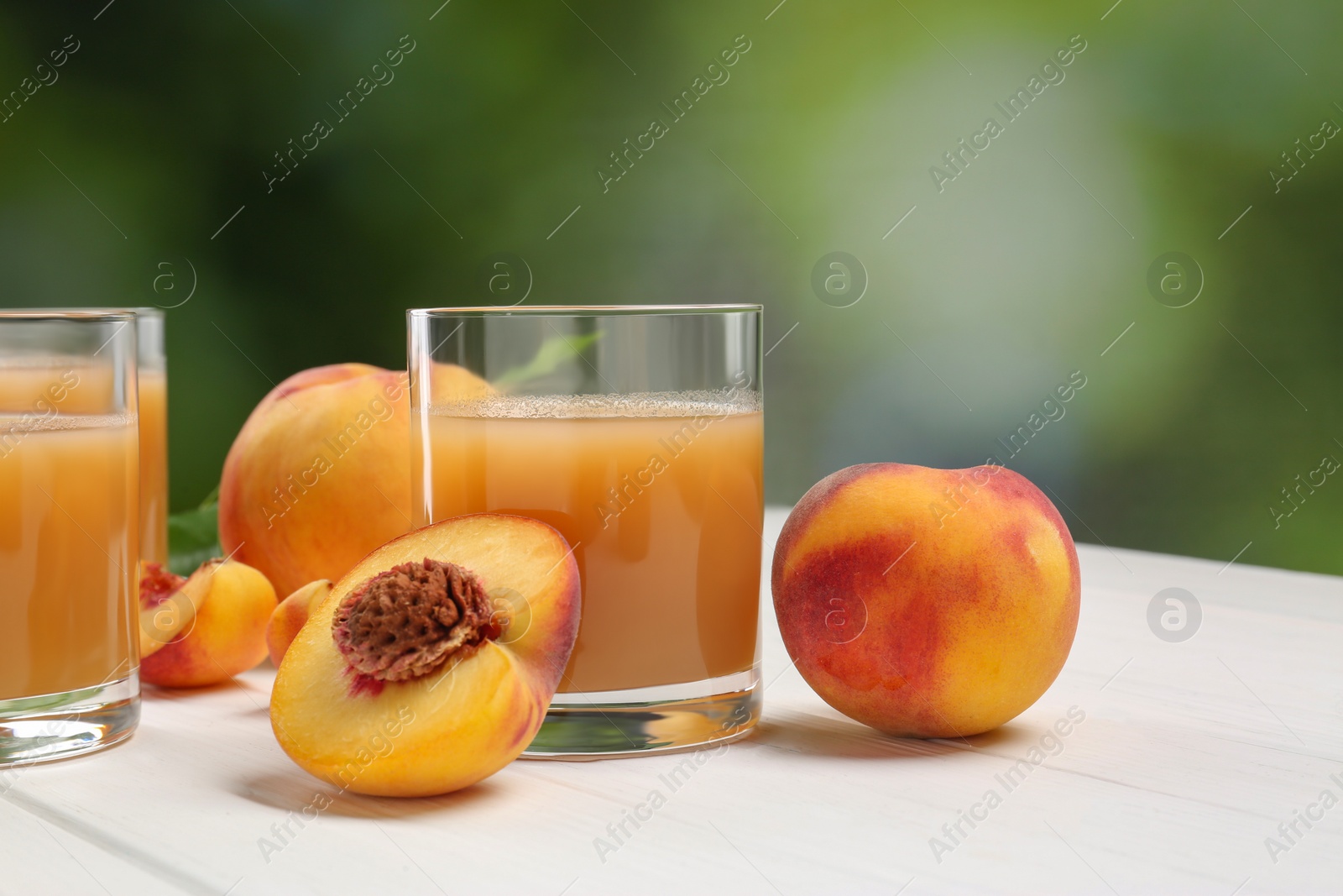 Photo of Glasses of peach juice and fresh fruits on white wooden table