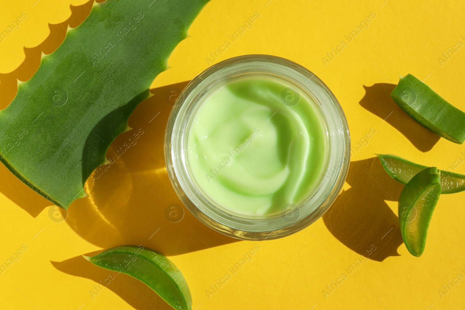 Photo of Jar with cream and cut aloe leaves on yellow background, flat lay