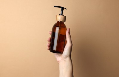 Woman holding bottle of cosmetic product on beige background, closeup