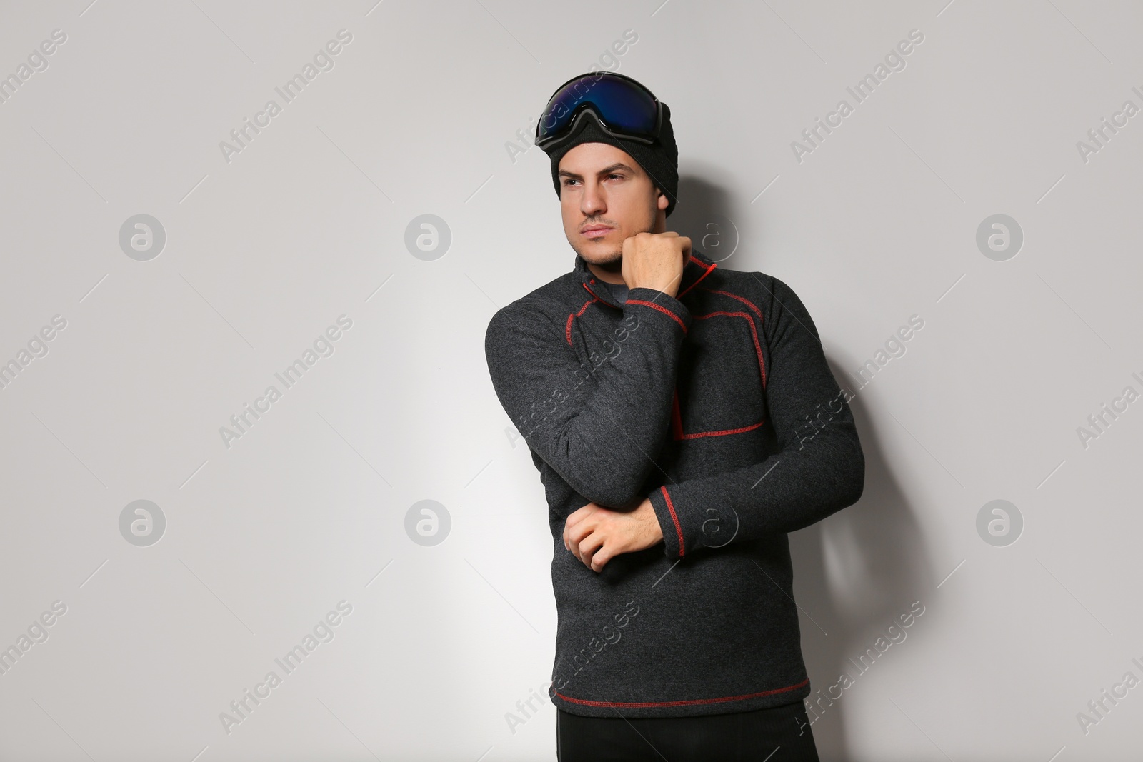 Photo of Man wearing fleece jacket and goggles on light grey background. Winter sport clothes