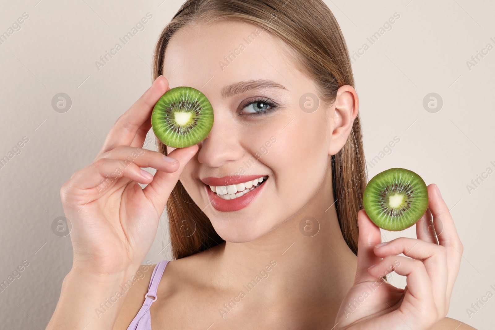 Photo of Young woman with cut kiwi on beige background. Vitamin rich food