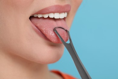 Woman brushing her tongue with cleaner on light blue background, closeup. Space for text