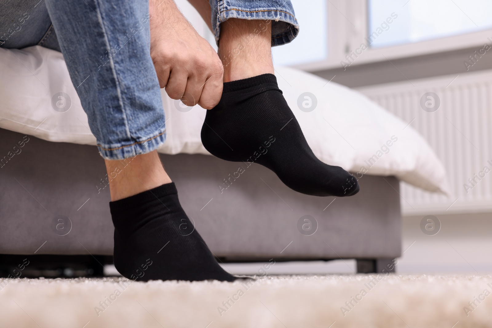 Photo of Man putting on black socks at home, closeup