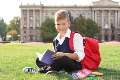 Photo of Schoolboy with stationery sitting on grass outdoors