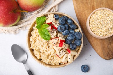 Bowl of delicious cooked quinoa with apples, blueberries and chia seeds on light grey table, flat lay