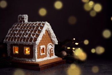 Photo of Beautiful gingerbread house decorated with icing on grey table against blurred festive lights