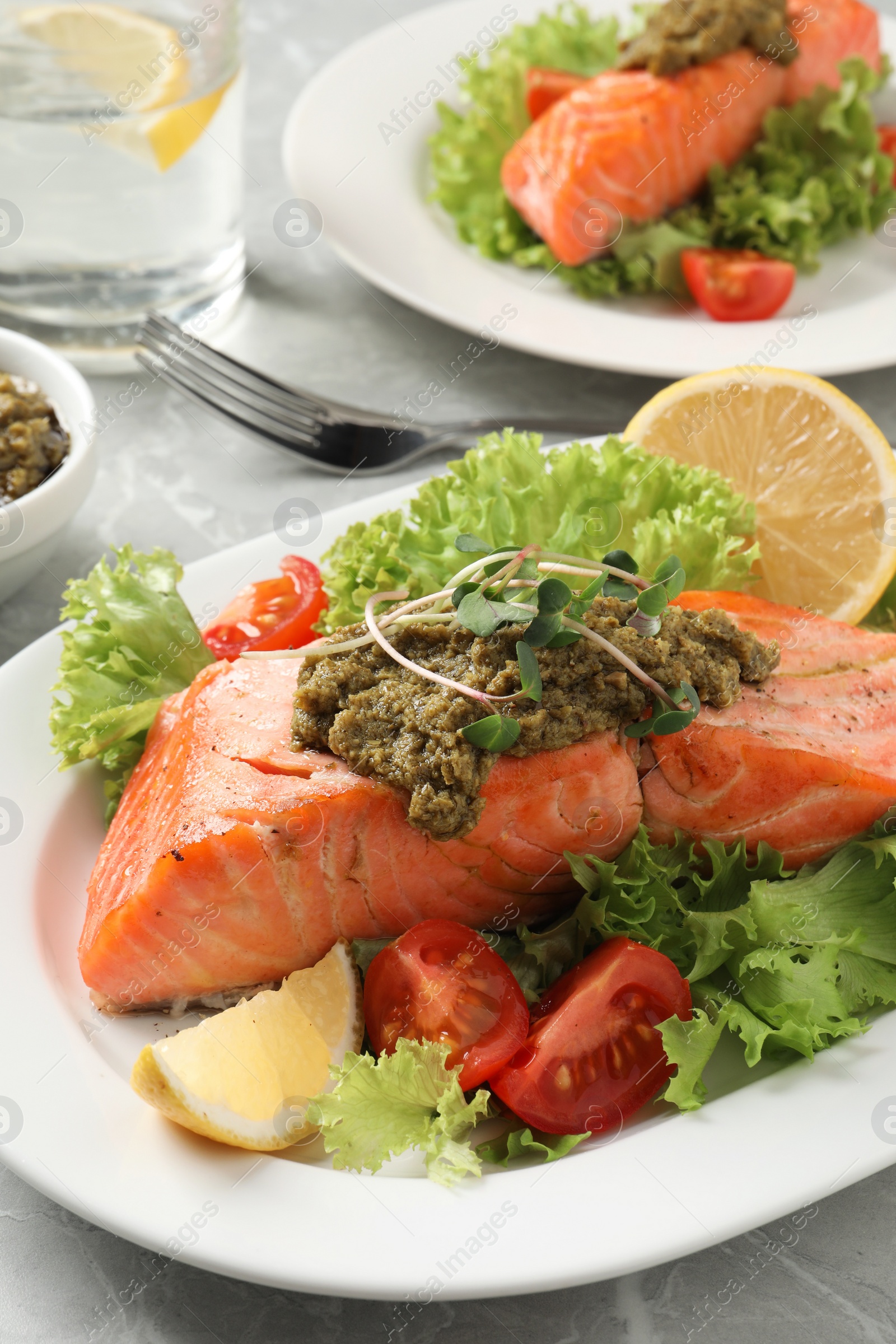 Photo of Tasty cooked salmon with pesto sauce and fresh salad served on grey table, closeup