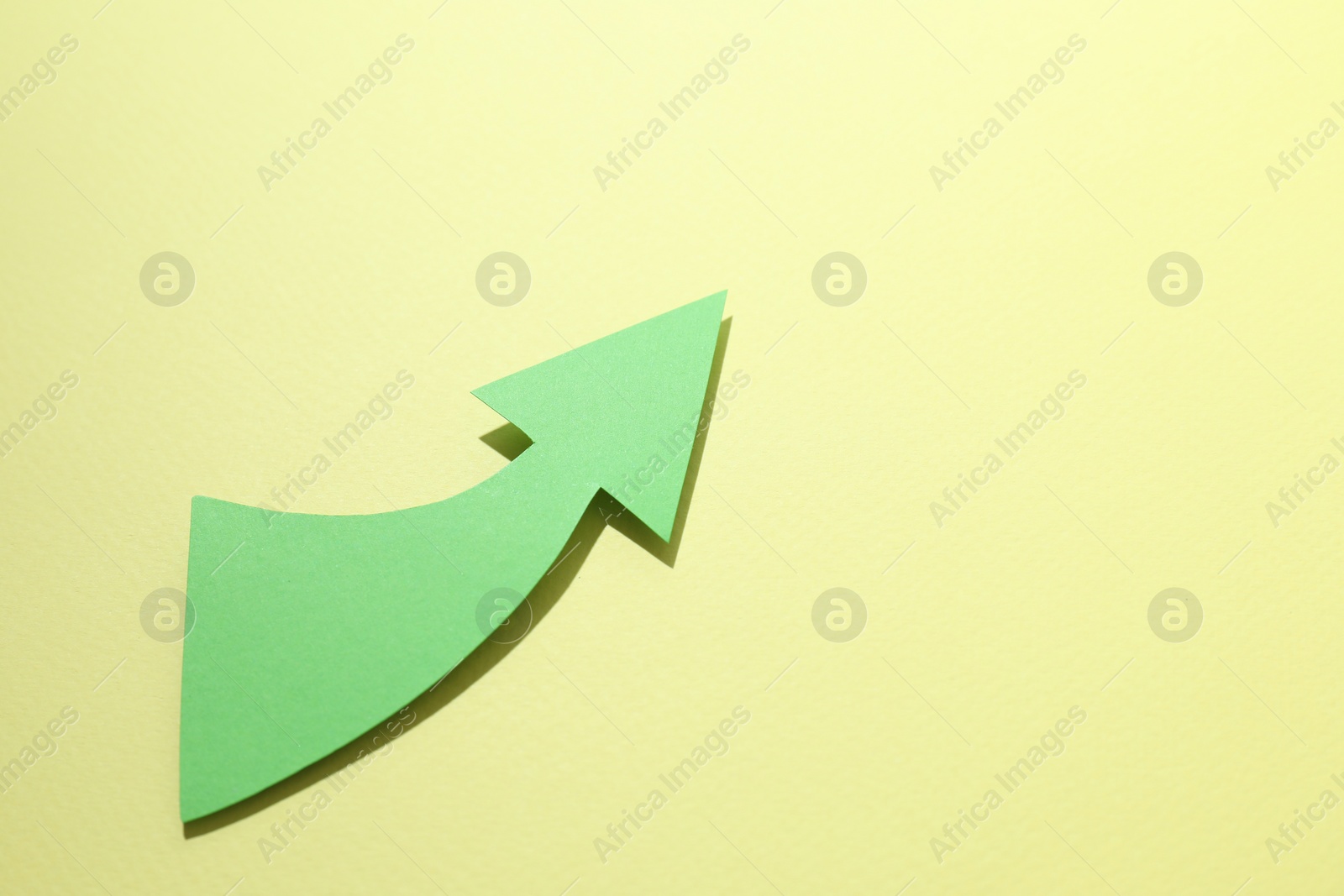 Photo of Curved green paper arrow on yellow background, top view. Space for text