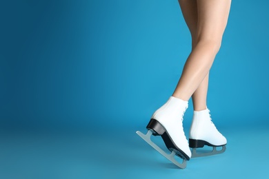 Photo of Woman in elegant white ice skates on light blue background, closeup of legs. Space for text