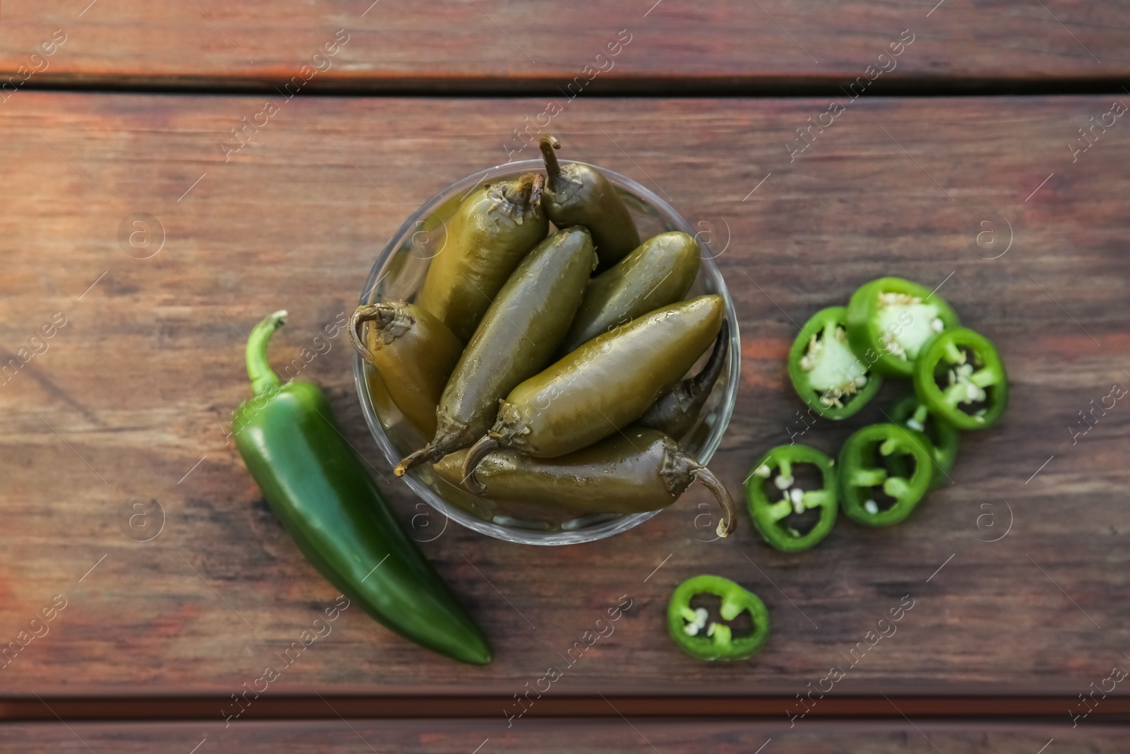 Photo of Fresh and pickled green jalapeno peppers on wooden table, flat lay