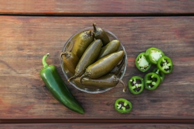 Photo of Fresh and pickled green jalapeno peppers on wooden table, flat lay