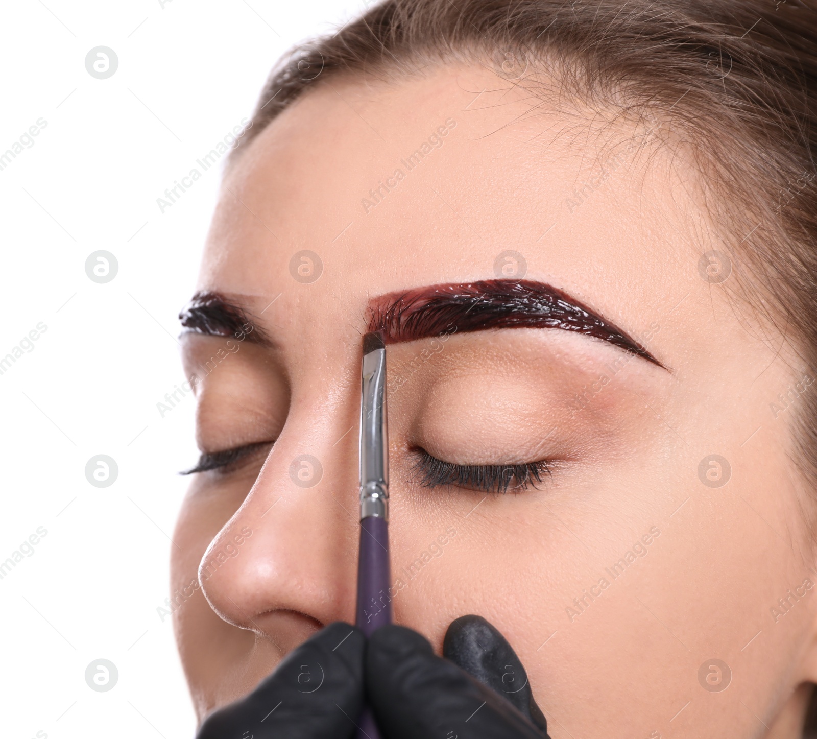 Photo of Beautician applying tint during eyebrows correction procedure on white background, closeup