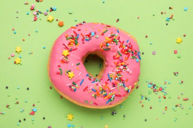 Photo of Glazed donut decorated with sprinkles on green background, top view. Tasty confectionery