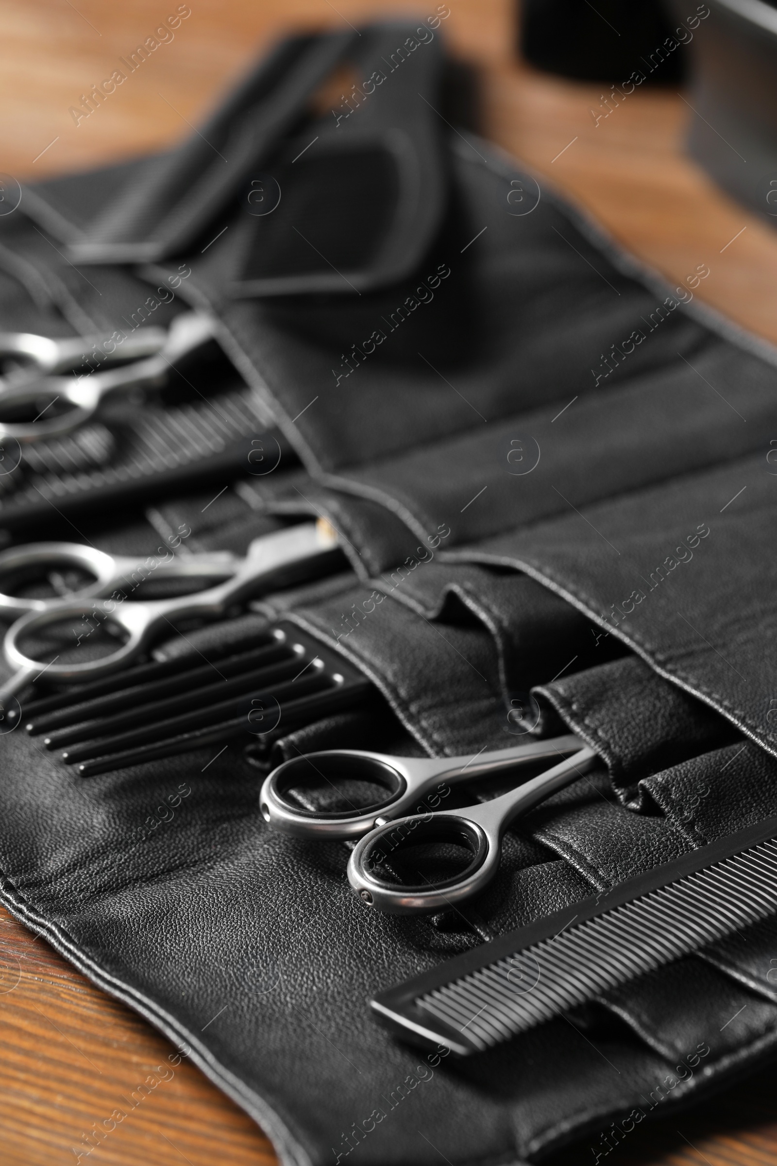 Photo of Hairdresser tools. Professional scissors and combs in leather organizer on wooden table, closeup