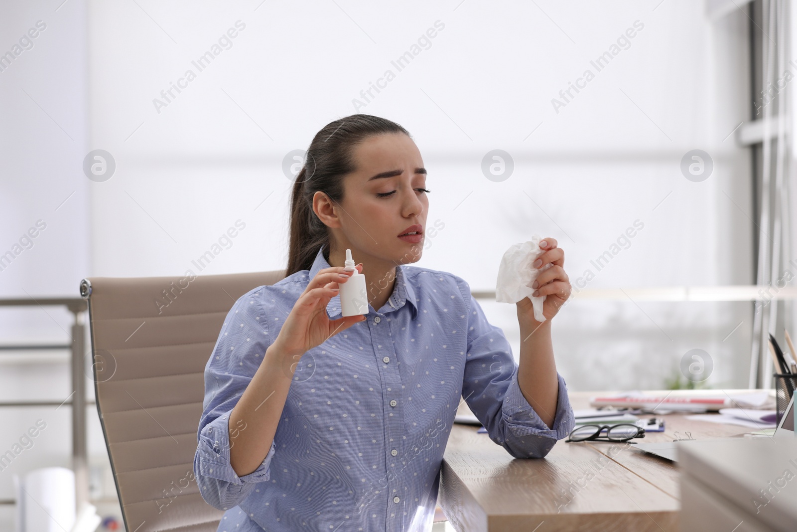 Photo of Sick young woman with nasal spray and napkin in office