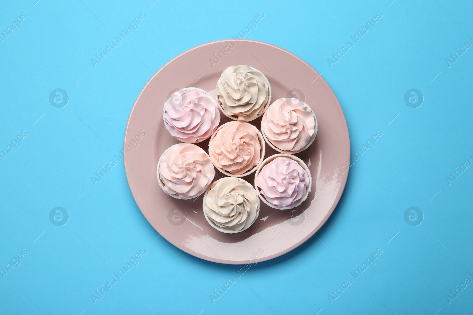 Photo of Plate with tasty cupcakes on light blue background, top view