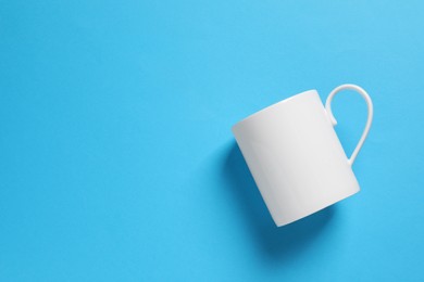 Photo of One white ceramic mug on light blue background, top view. Space for text