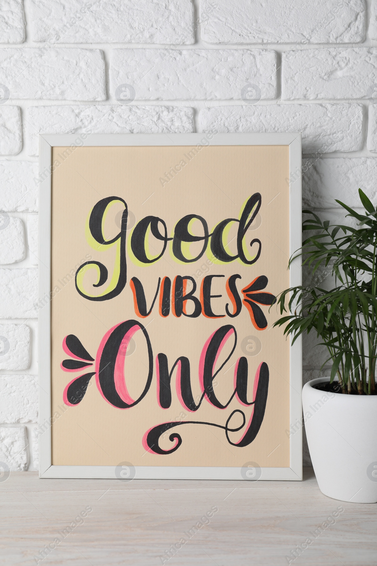Photo of Board with phrase Good Vibes Only and houseplant on wooden table near white brick wall