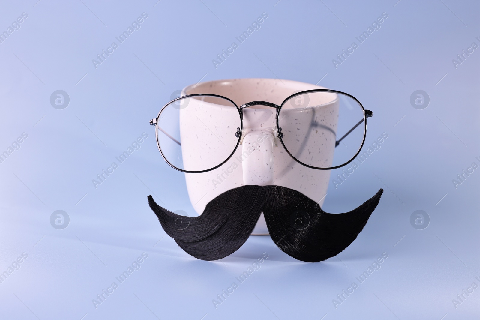 Photo of Man's face made of artificial mustache, glasses and cup on light blue background