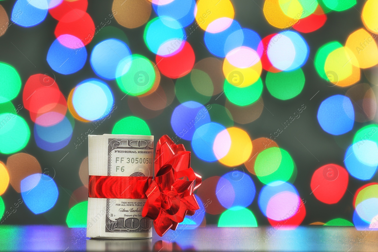 Photo of Dollar bills with gift bow on table against blurred lights, space for text. Bokeh effect