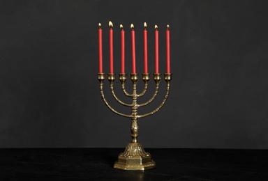 Photo of Golden menorah with burning candles on table against black background