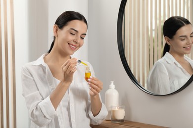 Photo of Young woman with bottle of essential oil indoors