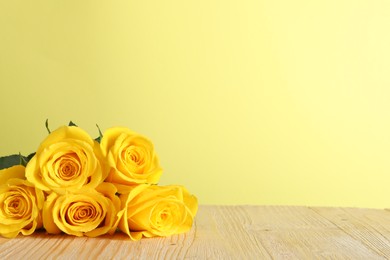 Beautiful fresh roses on wooden table against yellow background. Space for text