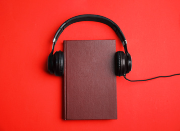 Book and modern headphones on red background, top view