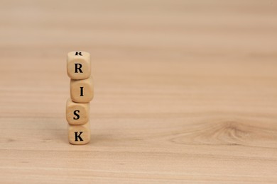 Photo of Stack of cubes with word Risk on wooden table. Space for text