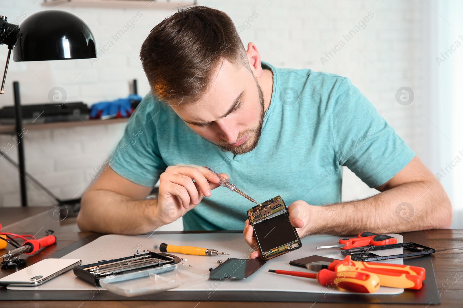 Photo of Technician repairing mobile phone at table in workshop