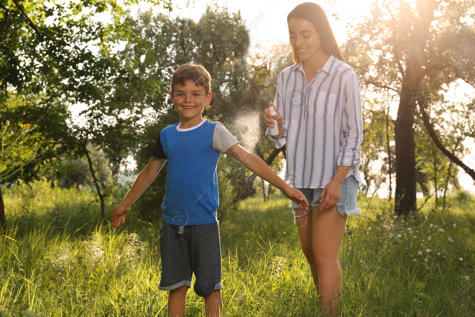 Photo of Woman applying insect repellent on her son's arm in park. Tick bites prevention