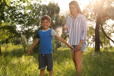 Woman applying insect repellent on her son's arm in park. Tick bites prevention