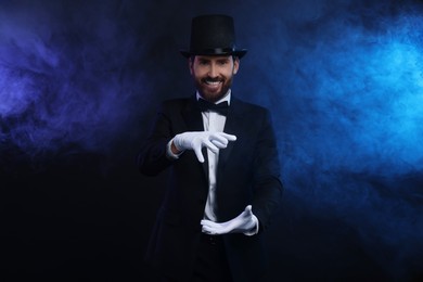 Photo of Happy magician holding something in smoke on dark background
