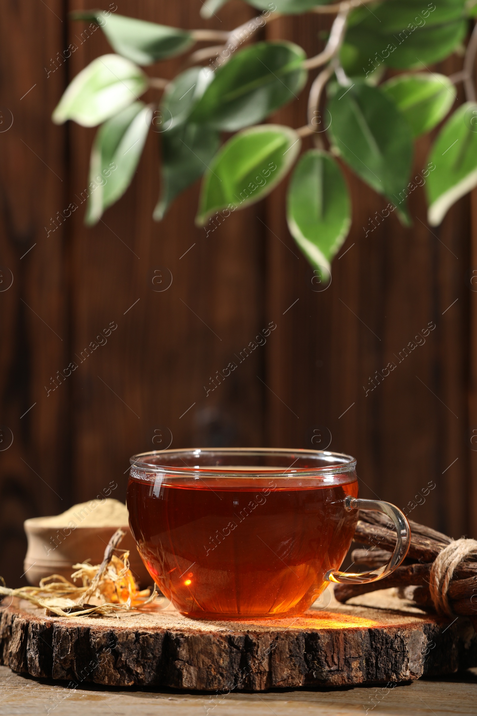 Photo of Aromatic licorice tea in cup and dried sticks of licorice root on wooden table, space for text