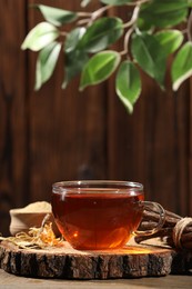 Photo of Aromatic licorice tea in cup and dried sticks of licorice root on wooden table, space for text