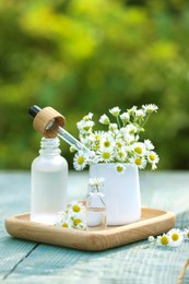 Photo of Bottles of chamomile essential oil, pipette and flowers on grey wooden table