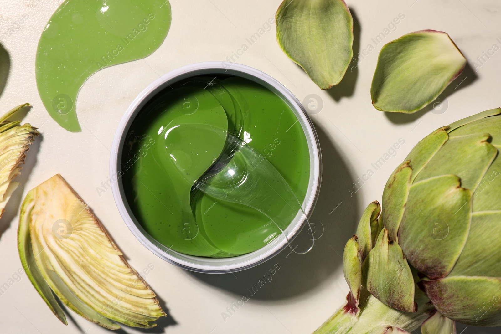 Photo of Package of under eye patches and artichokes on white table, flat lay. Cosmetic product