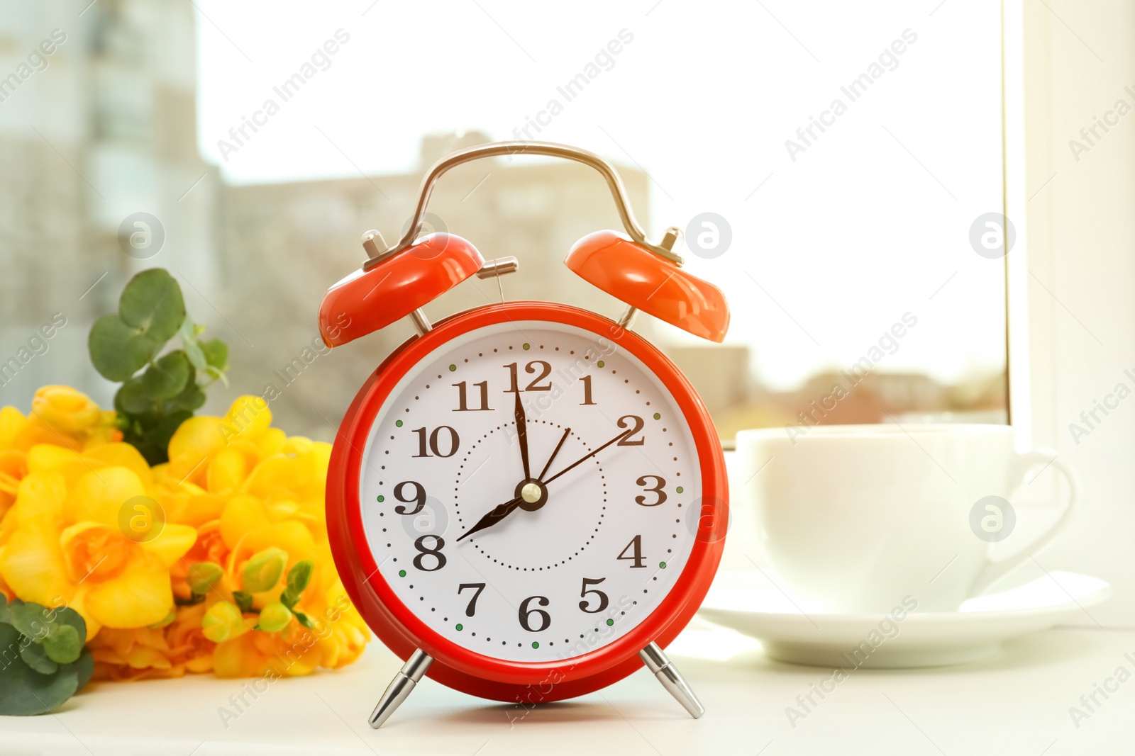 Photo of Alarm clock, beautiful yellow freesias and cup of drink on windowsill. Good morning