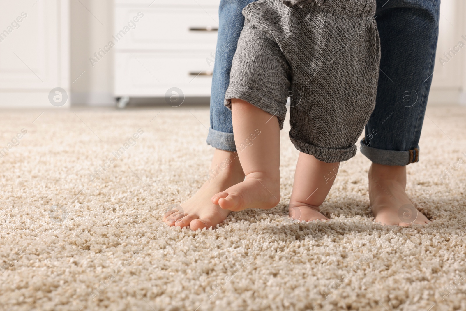 Photo of Mother supporting her baby son while he learning to walk on carpet at home, closeup. Space for text