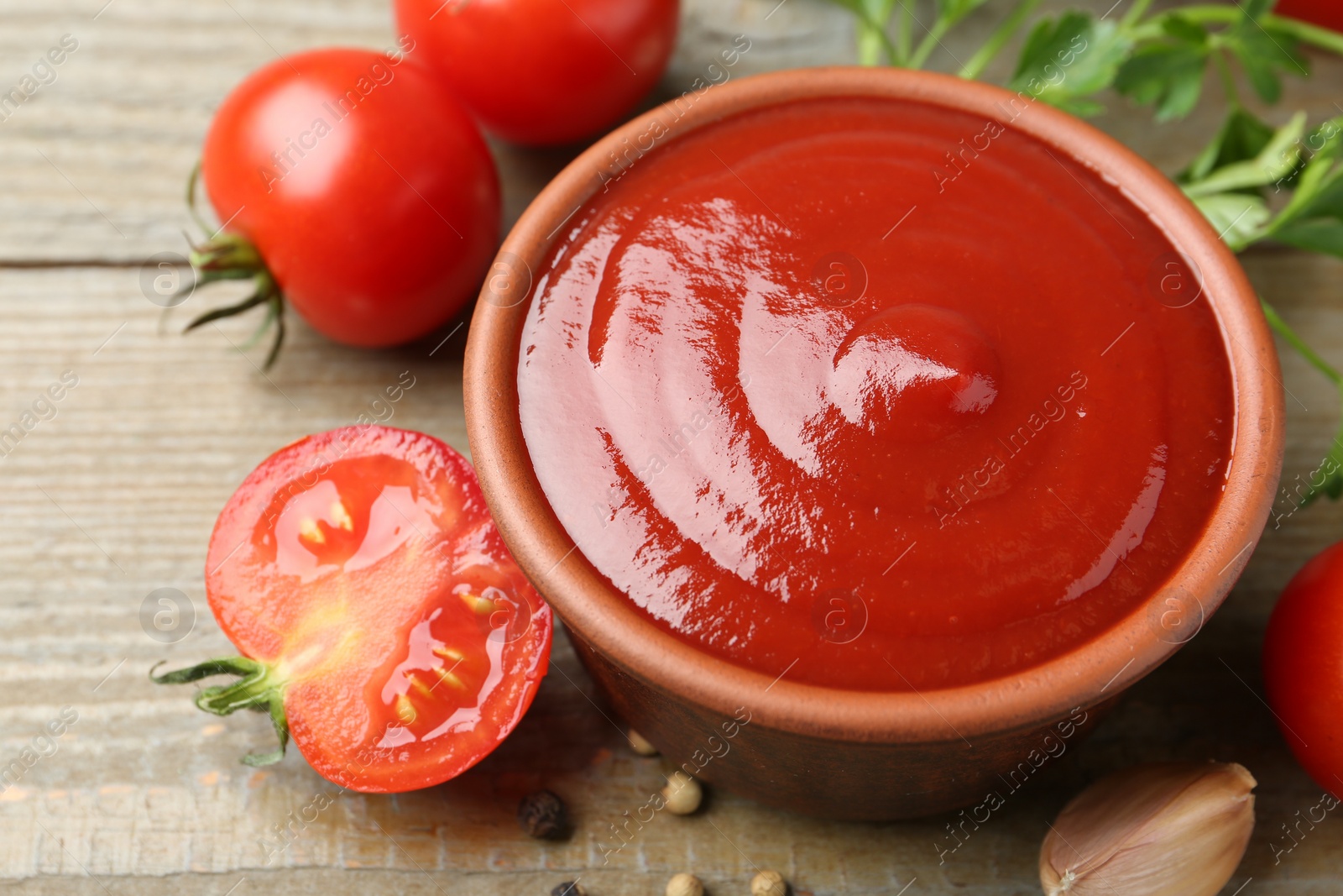 Photo of Tasty ketchup, fresh tomatoes, parsley and spices on wooden table, closeup