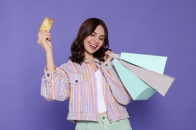 Beautiful young woman with paper shopping bags and credit card on purple background