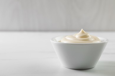 Photo of Tasty mayonnaise sauce in bowl on white table, closeup. Space for text