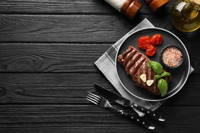 Photo of Delicious grilled beef steak served with spices and tomatoes on black wooden table, flat lay. Space for text