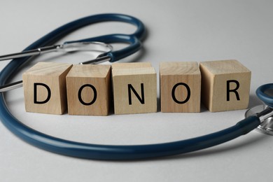 Word Donor made of wooden cubes and stethoscope on light grey table, closeup